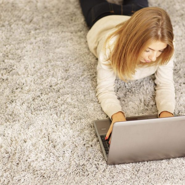 Happy young woman with laptop lying on the carpet at home